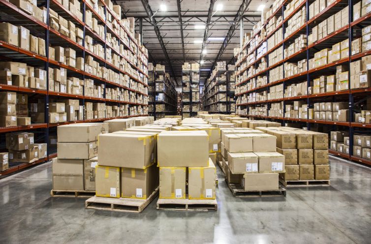 View down aisles of racks holding cardboard boxes of product on pallets in a large distribution warehouse