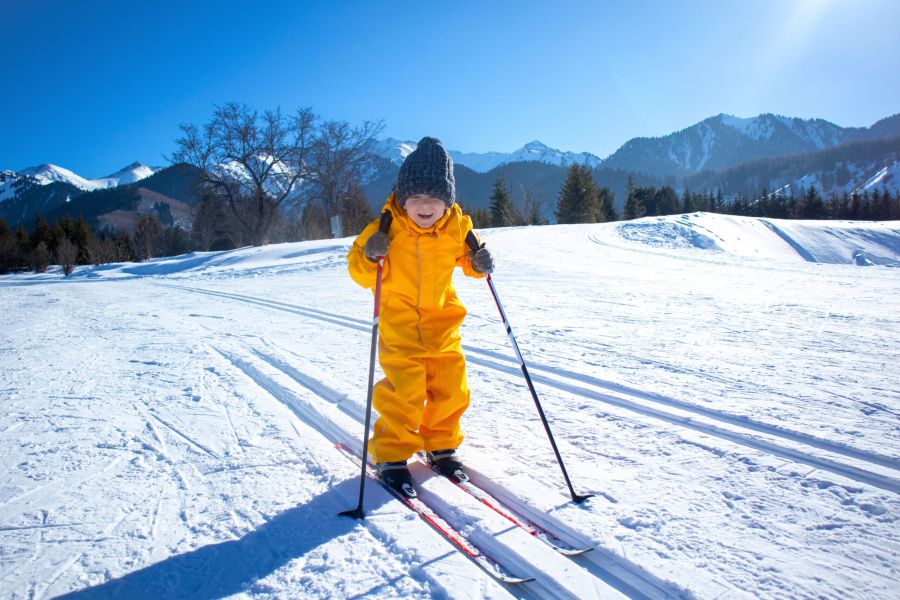 a little boy in a yellow jumpsuit on cross-country skiing
